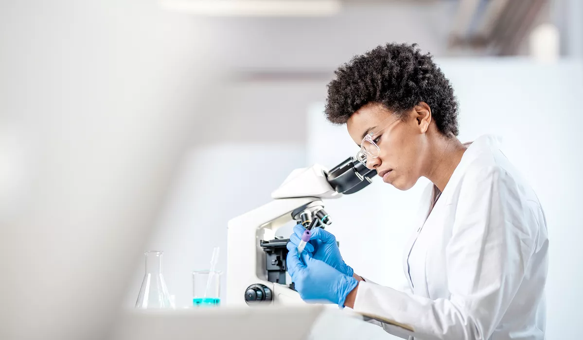 Woman scientist looking at specimen next to a microscope